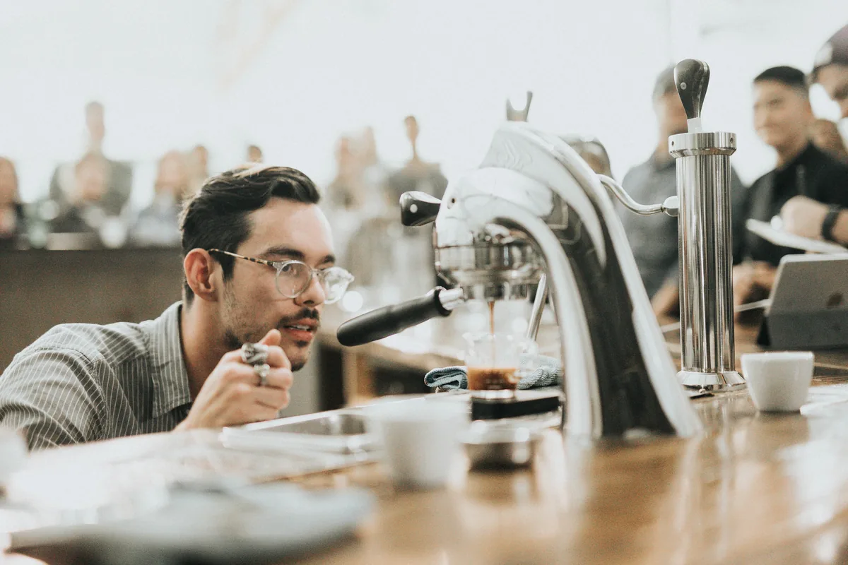 A barista at the espresso machine in a bright cafe